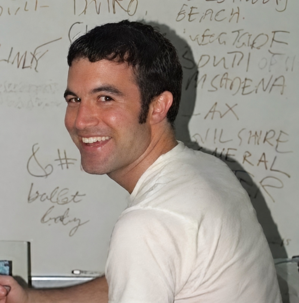 Portrait of a smiling man against a wall covered with handwritten notes.